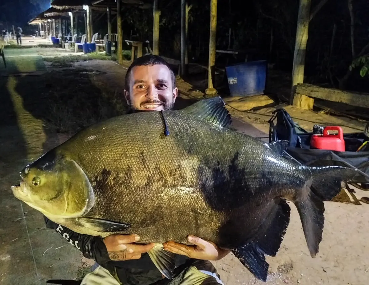 Pescador sorrindo com um tambaqui enorme à noite