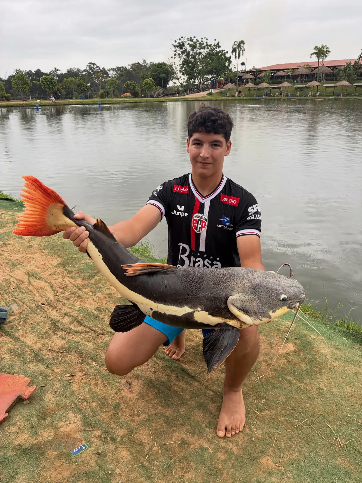 Jovem pescador segurando uma pirarara de cauda vermelha